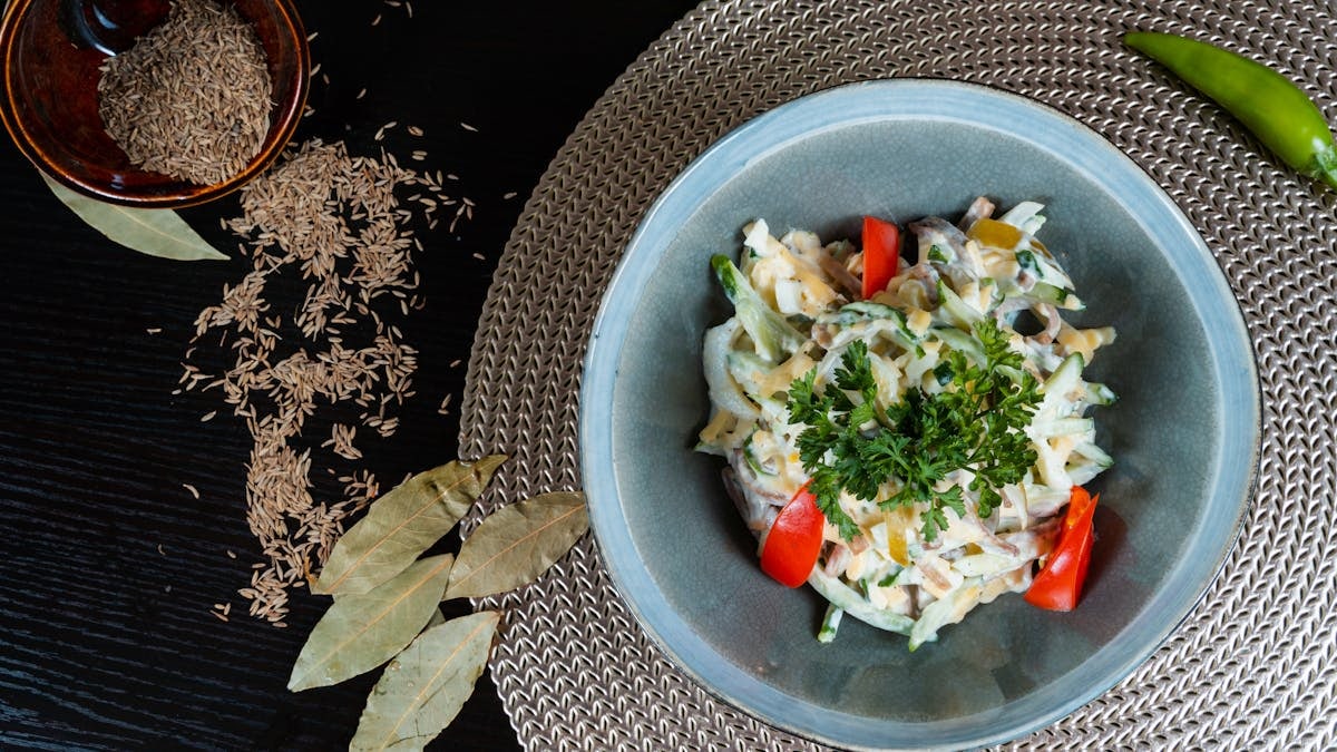 Fresh herb salad with tomatoes, cumin seeds, and spices on a woven mat.